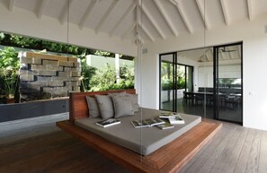 A modern bedroom with a built-in bed, a stone wall, and a view of a dining area.