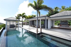 A modern poolside area with a clear pool, wooden deck, and lounge seating.