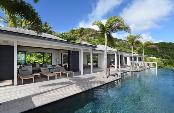 A modern resort with a poolside lounge area, a wooden deck, and a view of lush greenery.