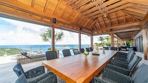 A spacious outdoor dining area with a wooden table and wicker chairs, overlooking a scenic ocean view.