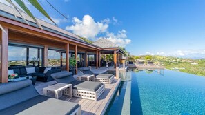 A modern outdoor pool area with lounge chairs and a wooden deck, overlooking a scenic landscape.