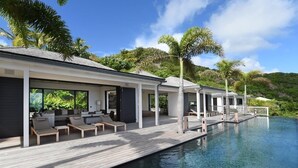 A modern resort with a poolside lounge area, a wooden deck, and a view of lush greenery.