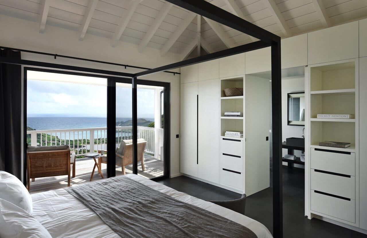 Una camera da letto con un grande letto, un balcone vista mare e armadi a muro bianchi.