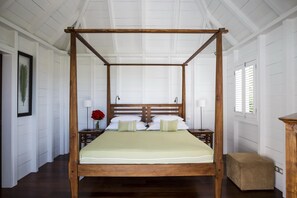Un lit à baldaquin avec un cadre en bois, deux tables de chevet avec des lampes, un vase avec des fleurs et un banc.