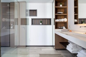Une salle de bain moderne avec une douche à parois de verre, un meuble-lavabo blanc doté d’une étagère en bois et des serviettes soigneusement pliées.