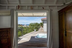 An open doorway leading to a wooden deck with a hot tub, overlooking a scenic view of boats and greenery.