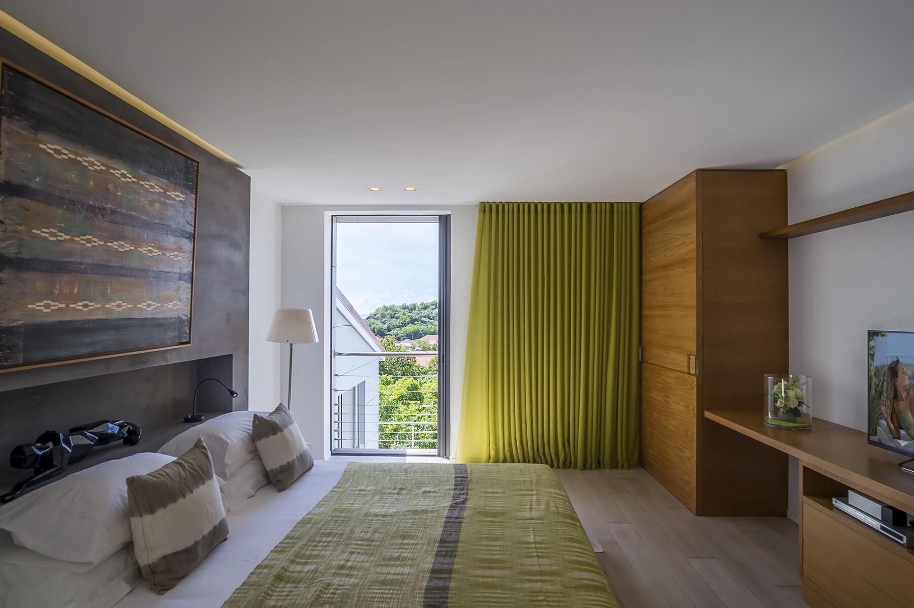 Une chambre moderne avec un grand lit, une vue sur la verdure par la fenêtre et une armoire en bois.