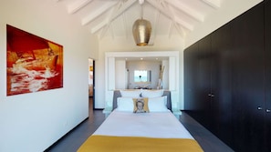 A modern bedroom with a large bed, a view of the sea, and a dark wardrobe.
