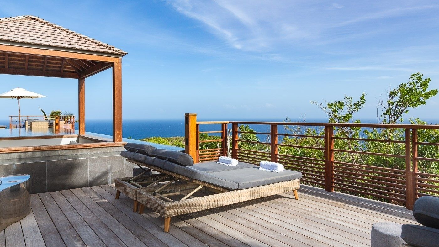A wooden deck with a lounge chair and a small table, overlooking a scenic ocean view.
