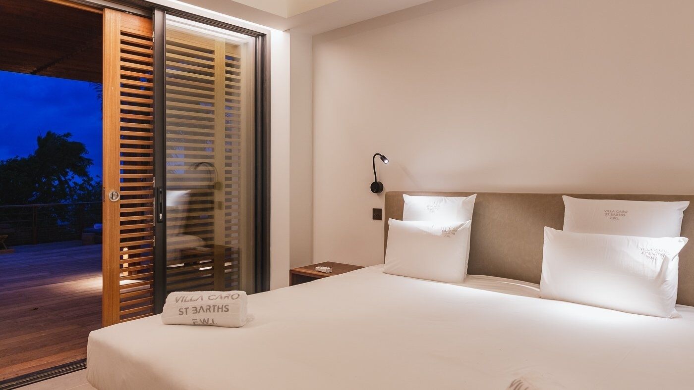 Une chambre d’hôtel comprenant un lit, une table de chevet, une lampe et une porte-fenêtre coulissante donnant sur un espace extérieur.