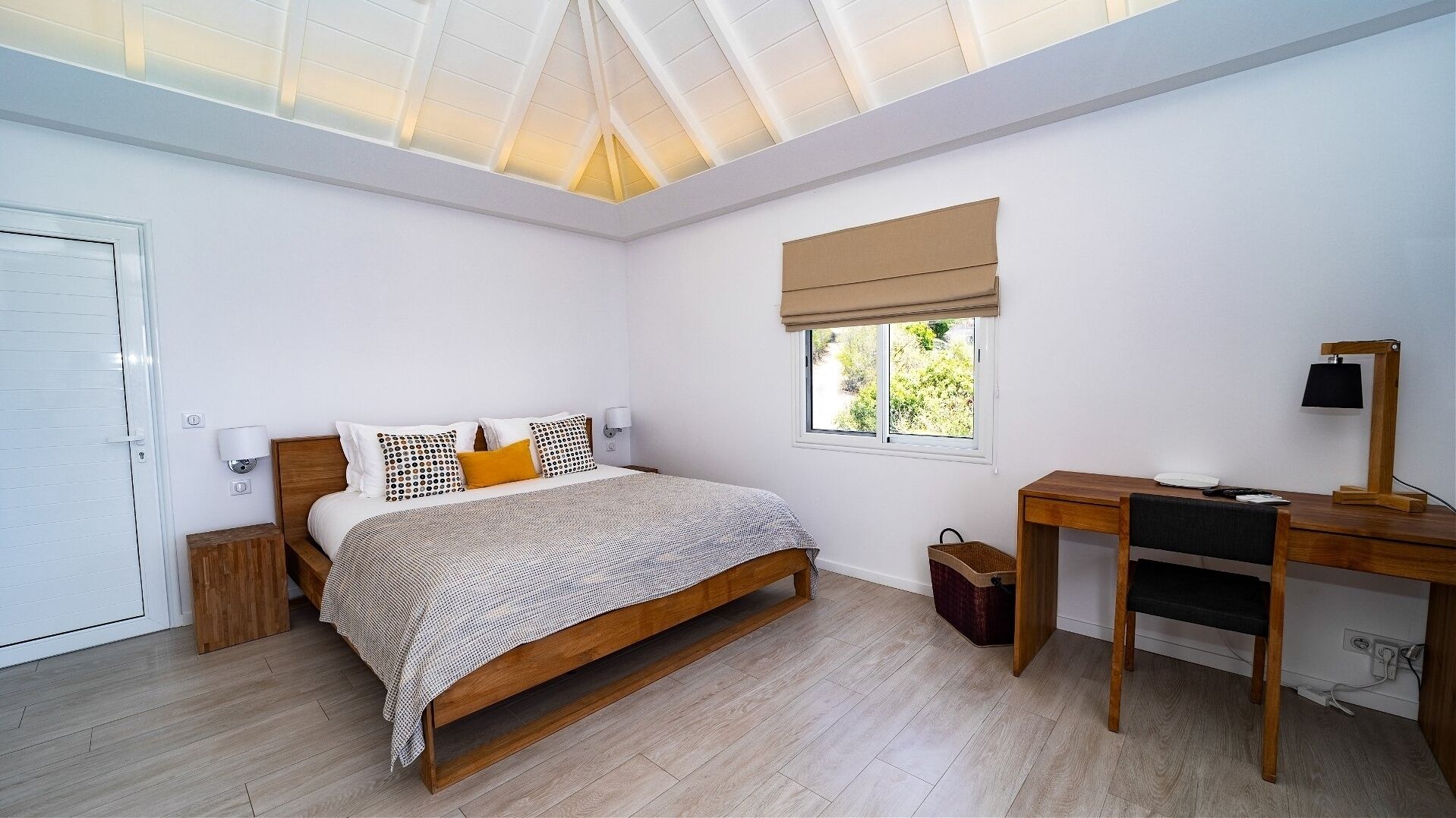 A bedroom with a bed, bedside table, lamp, desk, and window.