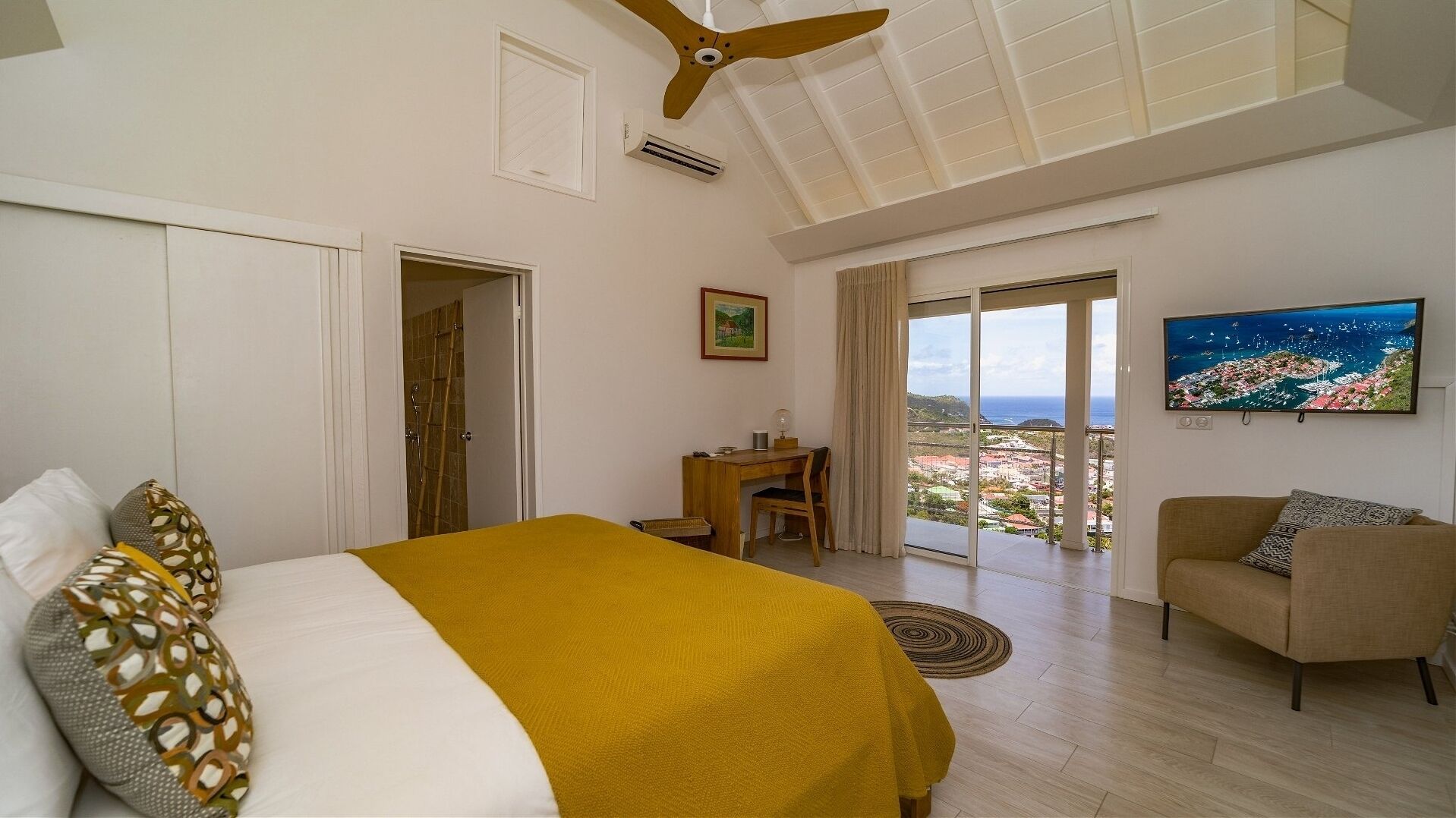 Un dormitorio con cama, escritorio, silla, sofá y televisor mostrando un paisaje.