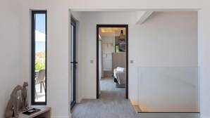 Passadís modern d'hotel amb vistes cap a l'exterior, un llit i un bany visible a través d'una porta oberta.