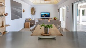 Ein modernes Wohnzimmer mit einem großen Esstisch aus Holz, Sofas, einem Fernseher und einer Topfpflanze.