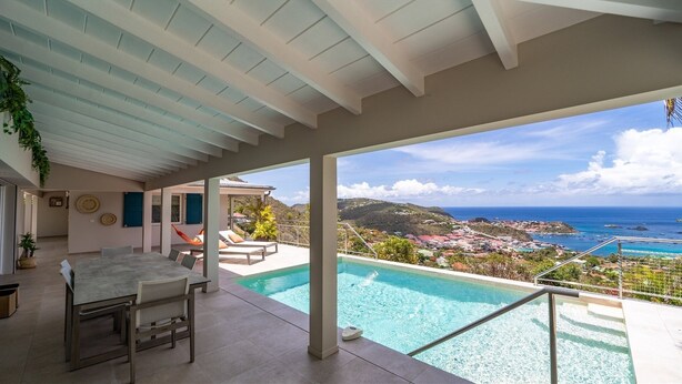 Ein überdachter Außenbereich mit Pool, Liegestühlen und Blick auf das Meer und die Stadt.