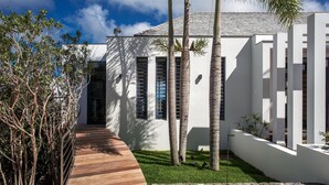 A modern house with a wooden deck, palm trees, and a white exterior. - Bastide (2/3 Rooms) Luxury villa (St Barts)