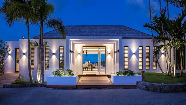 A modern house with a large glass door entrance, a flat roof, and a view of the ocean. - Bastide (2/3 Rooms) Luxury villa (St Barts)