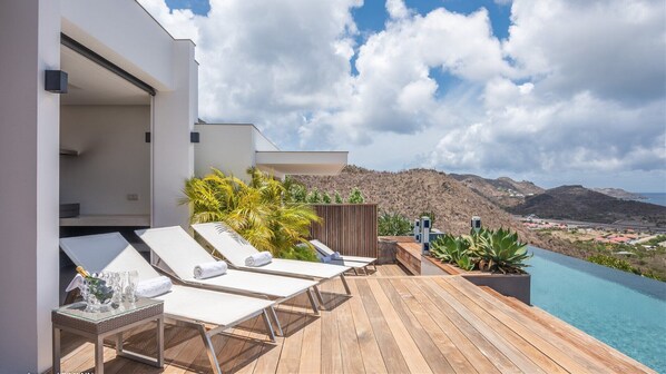 A wooden deck with lounge chairs and a pool overlooking a mountainous landscape.