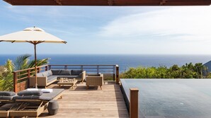 A wooden deck with outdoor furniture, a large umbrella, and a view of the ocean.