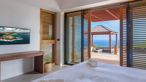 A bedroom with a bed, a TV, and a view of the ocean through large sliding doors.