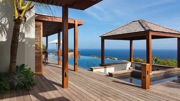 A wooden deck with a pool, a gazebo, and a view of the ocean.
