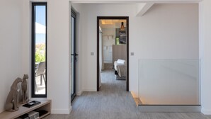 Ein moderner Hotelkorridor mit Blick ins Freie, ein Bett und ein durch eine offene Tür einsehbares Badezimmer.