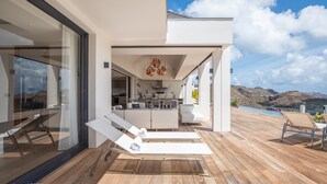 A modern outdoor living area with a pool, lounge chairs, and a kitchen visible through an open space. - Beautiful Bastide Luxury villa (St Barts)