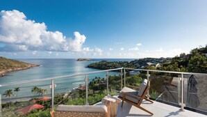Een balkon met uitzicht op zee, een stoel en een stenen tafel.