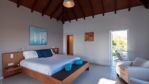 A bedroom with a wooden bed, a nightstand, a painting of sailboats, a colorful abstract painting, and a view of the outdoors through a glass door. - Bellevue (4/5 Rooms) Luxury villa (Marigot)