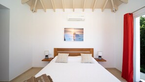 Una camera da letto con un letto grande, due comodini con lampade, una ventola a soffitto, una finestra con tende rosse e un condizionatore d'aria fissato al muro.