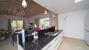 Una cucina moderna con un piano di lavoro in marmo nero, mobili bianchi e piano cottura integrato. C'è una zona pranzo con tavolo e sedie, e un'ampia finestra che offre luce naturale.