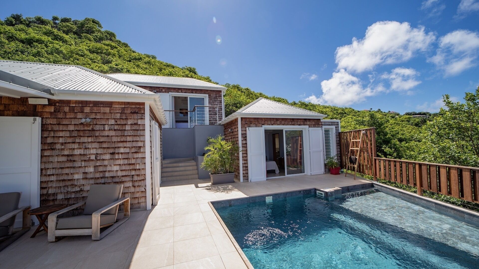 A modern house with a swimming pool, a covered patio, and a view of a lush green hillside.