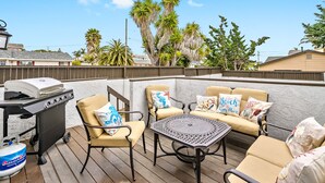 Une terrasse extérieure équipée d’un barbecue, de sièges et offrant une vue sur des palmiers.