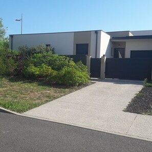 A modern building with a flat roof, a gravel driveway, and a metal gate.