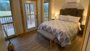 A bedroom with a bed, a bench, a ceiling fan, and a view through a door. - The Blue Door Cabin  (Winston-Salem)