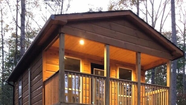 A two-story wooden cabin with a balcony, a door, and a small porch area. - The Blue Door Cabin  (Winston-Salem)