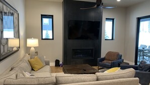 A modern living room with a sectional sofa, a coffee table, a fireplace, and a television. - Rare Find - Newer Construction close to town & beach! (Whitefish)