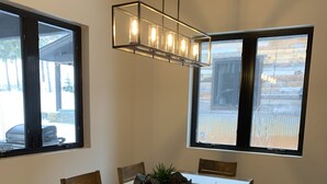 A dining area with a wooden table, chairs, a bench, a hanging light fixture, and large windows. - Rare Find - Newer Construction close to town & beach! (Whitefish)
