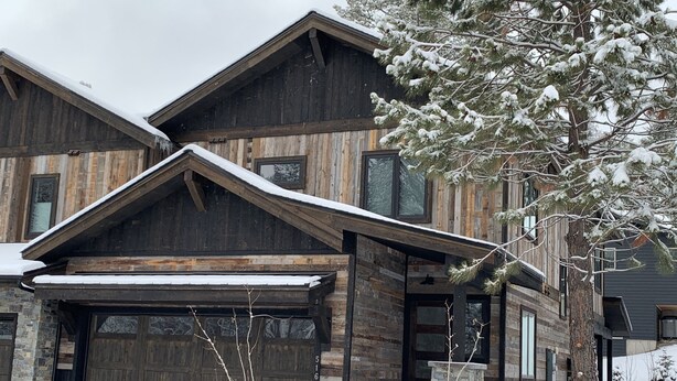 A large, rustic wooden house with a stone foundation, a garage, and a snow-covered landscape. - Rare Find - Newer Construction close to town & beach! (Whitefish)