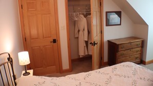 Ein Schlafzimmer mit Holztür, Kleiderschrank mit Kleidung, Kommode und Nachttischlampe.