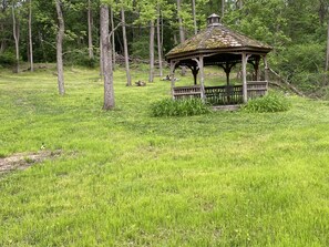 Un kiosque se dresse dans un champ verdoyant, entouré d’arbres.
