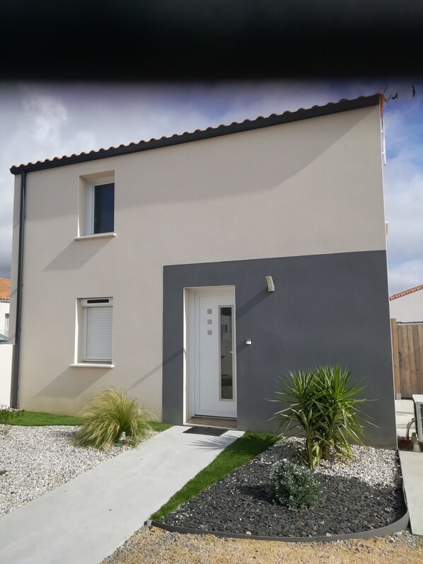 Una casa moderna de dos pisos con fachada blanca y gris oscuro, una puerta principal y un ventanal pequeño.