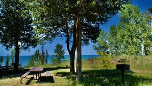 Un espace pique-nique avec un banc et un panneau indicateur, entouré d’arbres et offrant une vue sur la mer.