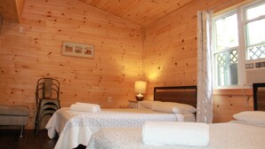 Une pièce de cabane en bois comprenant deux lits, une chaise, une table et une fenêtre avec des rideaux.