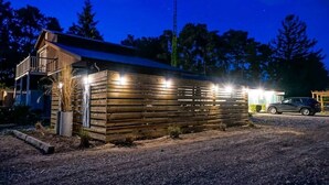 Une cabane en bois avec un balcon, une allée en gravier et une voiture garée.