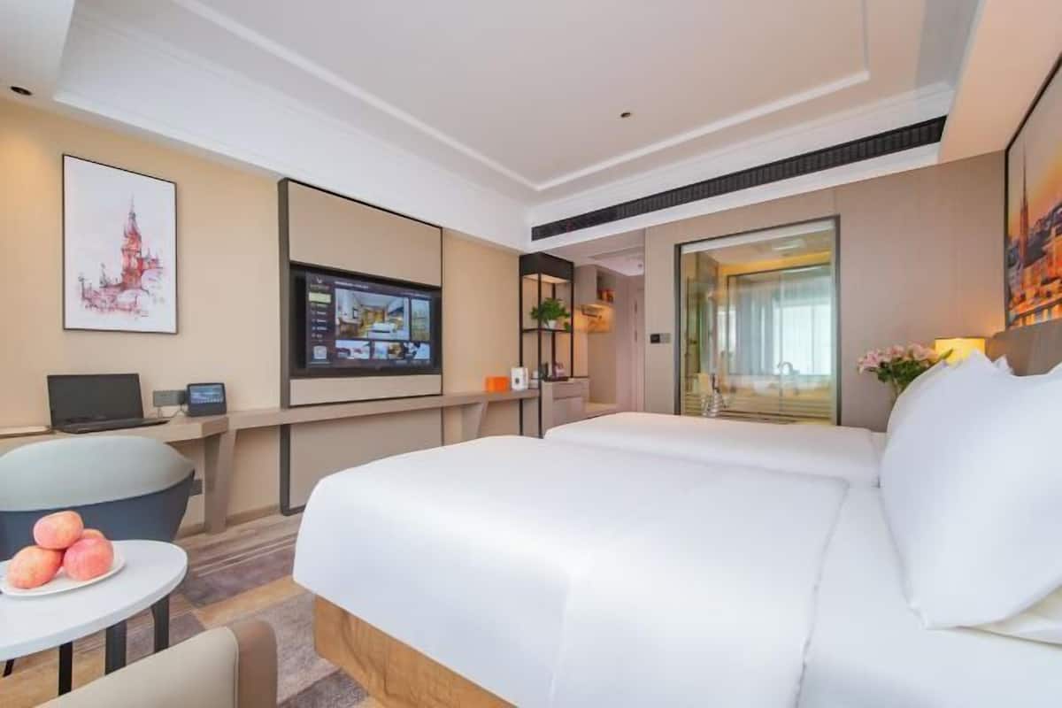 A hotel room with a bed, a desk with a computer, a small table with fruit, and a TV on the wall.