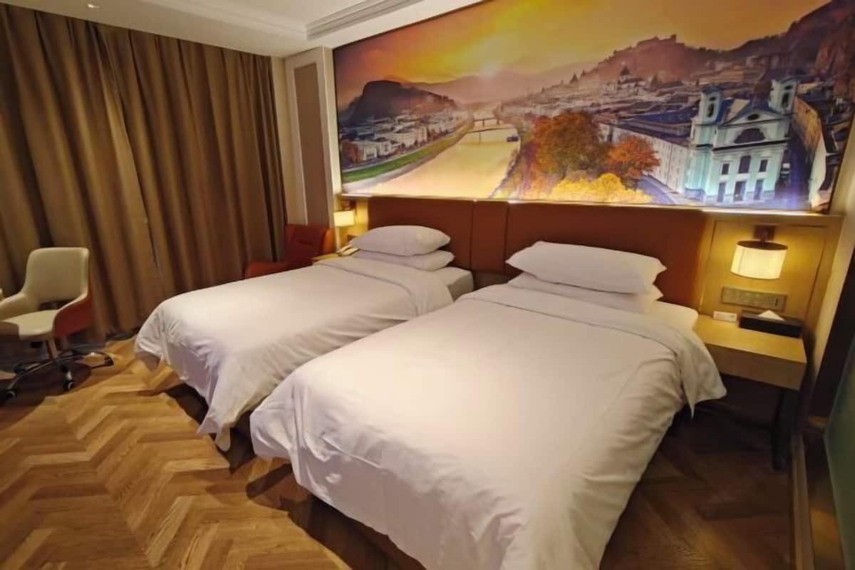 A hotel room with two beds, a wooden herringbone floor, a large mural of a cityscape, and a desk with a lamp.