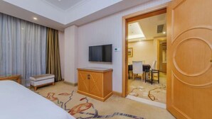 Een hotelkamer met een bed, een televisie, een houten kast, een bankje en een kamerbreed tapijt met dessin.