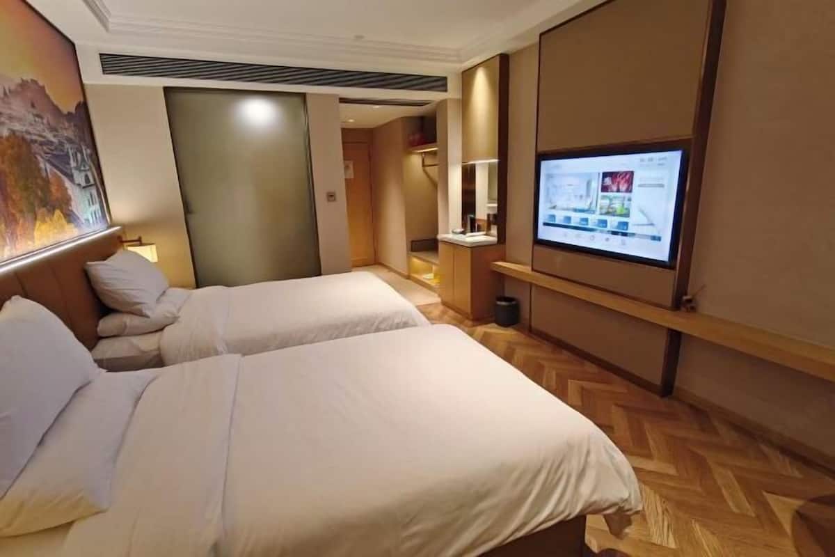 A hotel room with two beds, a TV, a desk, and a painting on the wall.