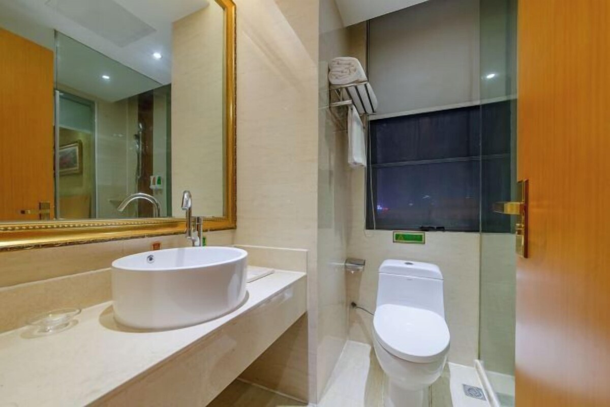 A modern bathroom with a large mirror, a round sink, a toilet, and a glass shower enclosure.